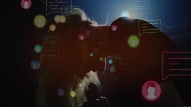 Müzik performansında mikrofona yaslanan bir kadın yüzen neon sohbet baloncuklarıyla etkileşime geçiyor. Siluet, neon, dijital, canlı, sürükleyici, konser, sosyal