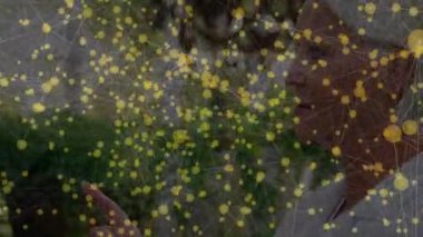 Bahçedeki sanal düğümlere dokunan son sınıf öğrencisi kadın dijital ağı parlayan bir kaplama ile sunuyor. Yaşlılar, açık hava, bağlantı, teknoloji, yenilik, canlılık, doğa