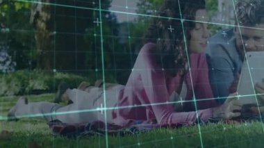 Parkta piknik battaniyesinde uzanan bir çift, animasyon veri grafikleriyle tablet teknolojisini izliyorlar. Açık hava, rahatlama, rahatlama, teknoloji, doğa, iletişim, gelişigüzel