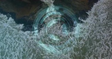 Kayalık kıyı şeridinin üzerinde yüzen fütüristik dijital HUD yüzeyi veri halkalarını ve okyanus şekillerini gösteriyor. Teknoloji, yenilik, denizcilik, macera, keşif, veri görselleştirme,