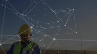 Güvenli yelek giyen mühendis ağ grafikleriyle örtülü tablet üzerindeki rüzgar çiftliği verilerini izliyor. Yenilenebilir enerji, dijital arayüz, açık hava etkinliği, profesyonel, sürdürülebilirlik, teknoloji, çevre