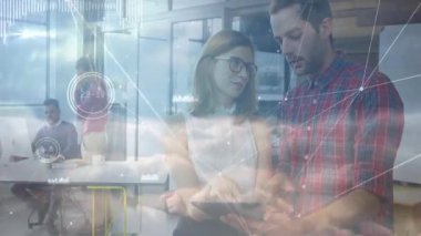 Ofiste tableti inceleyen iki iş arkadaşı, dizüstü bilgisayarı ve akıllı telefonu kaplayan teknoloji grafikleri. İşbirliği, dijital, yenilik, çalışma alanı, ağ oluşturma, üretkenlik, modern