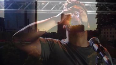 Erkek sunucu sahnede kulak monitörünü düzeltirken teknoloji şehir siluetlerini örtüyor. Konser, performans, şehir, ufuk çizgisi, modern, teknoloji, sahne