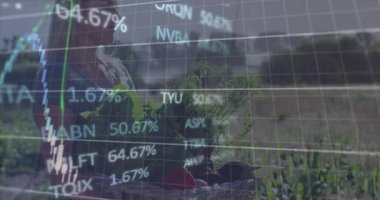 Bahçede elinde yeşil otlar tutan olgun bir kadın. Finans tabloları ve borsa saatleriyle örtüşüyor. Bahçıvanlık, sağlık, doğa, finans, sağlık, büyüme, açık hava