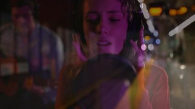 Şarkıcı kadın, müzik grafikleriyle tren istasyonunun ışıklarını birleştirirken mikrofona şarkı söylüyor. Müzik, işbirliği, kentsel, canlı, performans, gece hayatı, eğlence