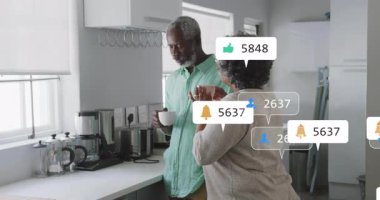 Mutfak tezgahında durmuş kupaların etrafında yüzen dijital pazarlama ölçümlerini seyreden yaşlı çift. Yaşam tarzı, yerli, çağdaş, uygulama, iletişim, sağlık, mutluluk