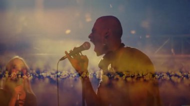 Erkek şarkıcı işaret ediyor, iki kadın vokalist müzik sahnesinde şarkı söylüyor, havada süzülen konfeti parıldıyor. Performans, eğlence, atmosfer, aydınlanma, kutlama, sanatçılık, gösteri dünyası