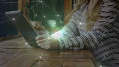 Teknoloji atölyesinde tablet kullanarak ahşap masada oturan yeşil ağ çizgileri olan bir kadın. Teknoloji, çalışma alanı, modern, yenilik, iletişim, basitlik, bağlantı