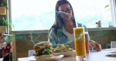 Kadın kafede hamburger ve avokado tostu tadıyor sosyal medya için animasyon menü ikonları sergiliyor. Günlük yemek, arkadaşlık, şehir kafesi, çağdaş tarz, doğal ışık, yemek fotoğrafçılığı, sosyal etkileşim