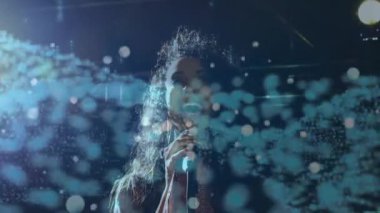 Stüdyo sahnesinde mikrofon tutan şarkıcı havada süzülen turkuaz bokeh ve kod ile müzik yapıyor. Performans, eğlence, dijital, soyut, enerjik, gece hayatı, sanatçı