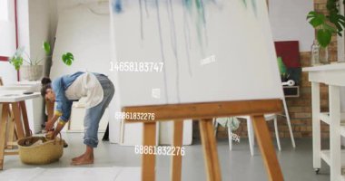 Sanat stüdyosunun zemininde eğilen kadın sanatçı, sepetin etrafında yüzen animasyon boya tüpleriyle. Yaratıcı, sanatsal, rustik, canlı, ilham verici, stüdyo, işçilik