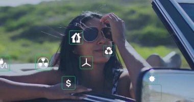 Kırmızı, üstü açık bir arabadan sarkan kırsal yolda gezen ve enerji teknolojisi ikonları sergileyen bir kadın. Macera, sürdürülebilirlik, seyahat, açık hava, modern, doğa, özgürlük