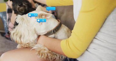 Pazarlama için yüzen sosyal medya ikonları sergilerken iki kadın koltukta teriyer köpeği tutuyor. Samimiyet, dostluk, rahatlama, yaşam tarzı, evcil, arkadaşlık, sevgi dolu.