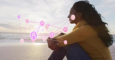 Gün batımında sahilde oturan bir kadın, yüzen kullanıcı simgeleriyle okyanus üzerinde teknoloji ağını sergiliyor. Manzara, sükunet, bağlantı, dinginlik, rahatlık, modern, derin düşüncelere dalma.