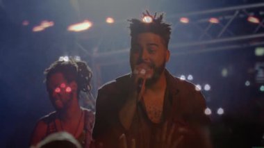 Konserde şarkı söyleyen ve gitar çalan iki müzisyen, animasyon müzik notaları ve soundbar eşliğinde. Göstericiler, eğlence, canlı, enerjik, sahne, seyirci, canlı