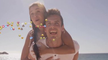 Adam sırtına biniyor ve kadın yüzen sosyal medya emojileriyle plajı işaret ediyor. Eğlence, dostluk, eğlence, yaşam tarzı, canlı, açık hava, bağlantı