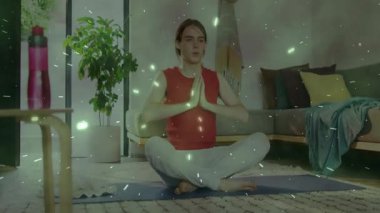 Evde su şişesi ve yüzen yeşil ışıklarla yoga minderi üzerinde meditasyon yapan bir kadın. Farkındalık, sükunet, rahatlama, dinginlik, doğal, çağdaş, yaşam tarzı