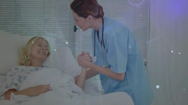 Sağlık hemşiresi hastanın üzerine eğilip el ele tutuşarak steteskopu panjurlarla gösteriyor. Bakım, şefkat, iyileşme, destek, konfor, profesyonellik, refah