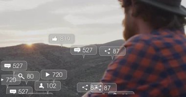 Gün batımında kayalık yamaçta oturan bir adam, yüzen sosyal medya pazarlama ikonlarıyla. Doğa, açık hava, tefekkür, engebeli, manzaralı, dijital, bağlantı