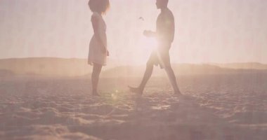 Çiftler gün batımında kumsalda diz çöküp pazarlama için yüzük kutusunun üzerinde animasyon kalp ikonu ile evlenme teklif ediyorlar. Romantizm, evlilik teklifi, aşk, bağlılık, günbatımı, sevgi, yakınlık