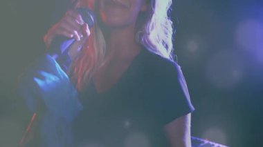 Sahnede şarkı söyleyen bir kadın, mikrofonda süzülen ses teknolojisi grafikleri ve renkli ışıklar. Performans, eğlence, konser, vokal, ışıklandırma, ruh hali, sahne