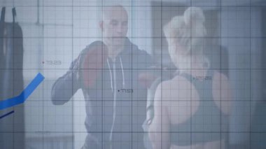 Spor salonunda odaklanma eldivenlerini yumruklayan antrenör. Şebeke çizelgesi de fitness ölçümlerini gösteriyor. Fitness, antrenman, güç, motivasyon, performans, sağlık, egzersiz