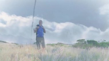 Orta yaşlı yürüyüşçü sırt çantasını ayarlıyor, yüzen kalp atış hızı grafiğini izliyor. Macera, keşif, açık hava, fitness, sağlık, manzara, aktivite