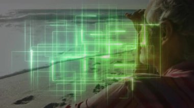 Kıdemli adam kumlu sahilde dürbün tutuyor, teknoloji için yeşil dijital şebeke örtüleri sergiliyor. Son sınıf, keşif, yenilik, viral, dijital, fütüristik, açık hava