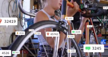 Kadın tamirci, atölyede turuncu bisiklet gidonu ayarlıyor. Teknoloji yüzen bildirimleri gösteriyor. Tamirci, tamirci, atölye, araçlar, şehir, bakım, sanayi