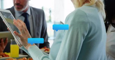 Kadın ofiste tablet tıklatırken, adam cihazı inceliyor, sohbet baloncukları ve teknik veriler gösteriyor. İşbirliği, teknoloji, iletişim, çalışma alanı, yenilik, dijital, üretkenlik