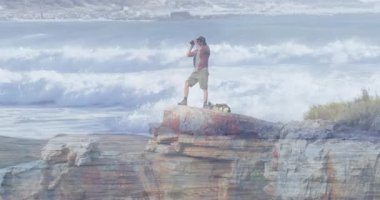 Kayalık sahil şeridinde deniz verilerinin üzerinde yüzen animasyon teknolojisi haritalarıyla ufku tarayan bir adam. Macera, keşif, engebeli, deniz, vahşi doğa, keşif, manzara