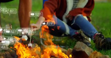 Orman temizliğinde kamp ateşiyle el ısıtan kampçılar, yüzen sosyal medya ikonlarının yer aldığı. Macera, açık hava, rahatlama, bağlanma, doğa, kırsal, boş zaman