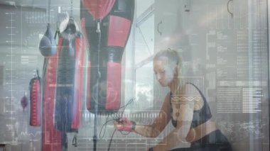 Spor salonundaki kum torbasının yanında ip atlayan bir kadın dijital fitness çizelgeleri sergiliyor. Fitness, eğitim, yenilik, güç, sağlık, dijital, motivasyon