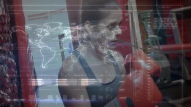 MMA spor salonunda ağır torba yumruklayan bir kadın holografik fitness veri akışı ve dünya haritası sergiliyor. Eğitim, fitness, teknoloji, mücadele, güç, egzersiz, motivasyon