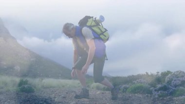 Yetişkin bir erkek yürüyüşçü, diz çöküp dağ yolunda bağcıklarını bağlıyor, sırt çantasının üstünde seyahat ediyor. Macera, keşif, vahşi doğa, açık hava, engebeli, yürüyüş, doğa.