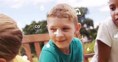 Çocuklar parktaki ahşap bankta ekolojik verileri tartışıyor, animasyon komutanları ve geri dönüşüm simgelerini gösteriyor. Oyunculuk, işbirliği, gençlik, doğa, sürdürülebilirlik, açık hava, öğrenme