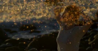 Kayalık plajda kollarını kaldıran kadın beyaz örgü örüyor, sağlık için altın çengeller takıyor. Doğal, sükunet, bohem, huzurlu, günbatımı, zarafet, tasasız