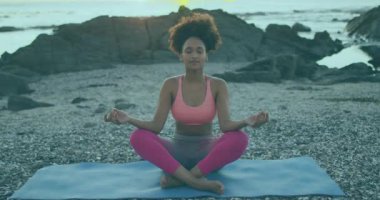 Plajda yoga minderi üzerinde meditasyon yapan bir kadın, sağlık için dijital beyin aktivitesi parçacıkları gösteriyor. Dinginlik, farkındalık, dijital, enerji, refah, doğa, soyut