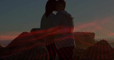 Günbatımında kayalık sahil şeridinde öpüşen çift, kırmızı ızgara animasyonuyla teknoloji verilerini gösteriyor. Romantizm, bağlantı, dinginlik, teknoloji, dijital, açık hava, manzara