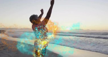 Sunset 'te plajda gerinen yaşlı bir kadın, yüzen turkuaz parçacıklarla sağlık teması gösteriyor. Dinginlik, sağIık, farkındalık, sükunet, rahatlık, açık hava, sakinlik.