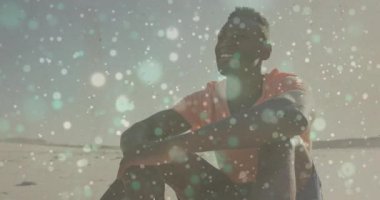 Sahilde bağdaş kurmuş oturan bir adam, pazarlama işleri için animasyon ışıkları sergiliyor. Rahatlama, rahatlama, sükunet, açık hava, canlı, rahat, yaşam tarzı.