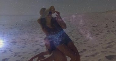 Sahilde poz veren erkek ve kadın hasır şapka ikonu ve nebula grafiklerini teknolojiyle örtüyor. Yaz, macera, rahatlama, manzara, coşku, eğlence, doğa.