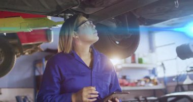 Otomotiv tamir atölyesinde kaldırma kolu altında tablet kullanan kadın tamirci, canlandırma veri simgeleriyle. Otomotiv, teknisyen, sanayi, modern, atölye, yenilik, bakım