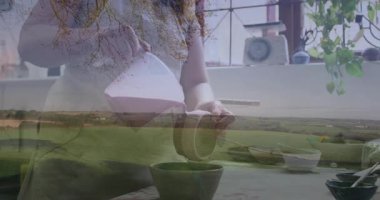 Orta yaşlı bir kadın yemek sahnesinde kaseye süt dökerek canlandırılmış tarım arazisi örtüsü sergiliyor. Aşçılık, mutfak, çiftlik evi, yaşam tarzı, yerli, aşçı, kırsal