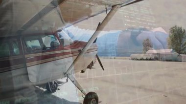 Pilot havaalanı önlüğündeki hangar kapısını açıyor. Dijital finansal grafikler uçağın üzerinde yüzüyor. Havacılık, lojistik, ulaşım, modern, teknolojik, endüstri, seyahat