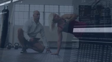 Müşteri spor salonunda kettlebell kenarı döşemesi yapıyor, antrenör diz çöküp tablet kontrol ediyor, sağlık çizelgesi çiziyor. Fitness, antrenman, güç, sağlık, spor, motivasyon, egzersiz