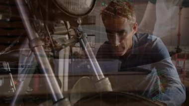 Mühendis atölyedeki motorsiklet süspansiyon tüpünü inceliyor, üst üste yerleştirilmiş borsa grafiklerini gösteriyor. Mekanik, endüstriyel, teknik, mühendislik, atölye, analitik, hassasiyet