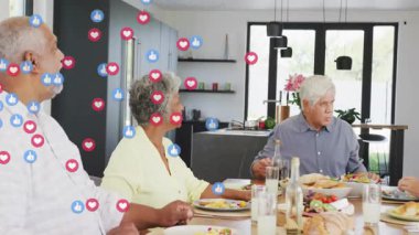 Modern mutfak masasının etrafında yüzen sosyal medya reaksiyon ikonlarıyla yemek paylaşan altı kişi. Aile, sosyal toplantı, modern iç mekan, aşçılık, kutlama, bağlantı, neşe