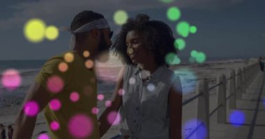 Deniz kıyısındaki sahil yolunda metal parmaklıklar ve bokeh ışıkları olan bir çifti gösteren bir seyahat kampanyası. Romantik, boş, hareketli, manzaralı, kaygısız, açık havada, genç.