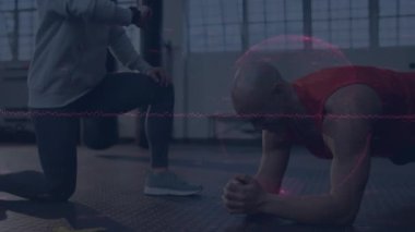 Fitness antrenörü diz çökmüş, zeka kontrolü yapıyor, müşterisi spor salonunda ön kol tahtasını tutuyor ve veri örtüyor. Sağlık, sağlık, güç, eğitim, teknoloji, motivasyon, spor